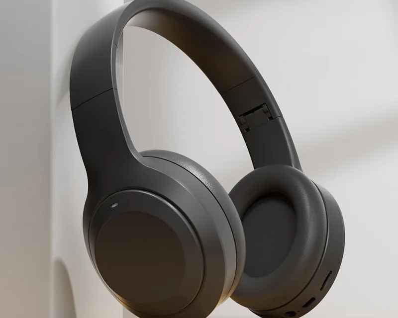 Dark gray over-ear wireless headphones resting on a light wood surface against a white wall.