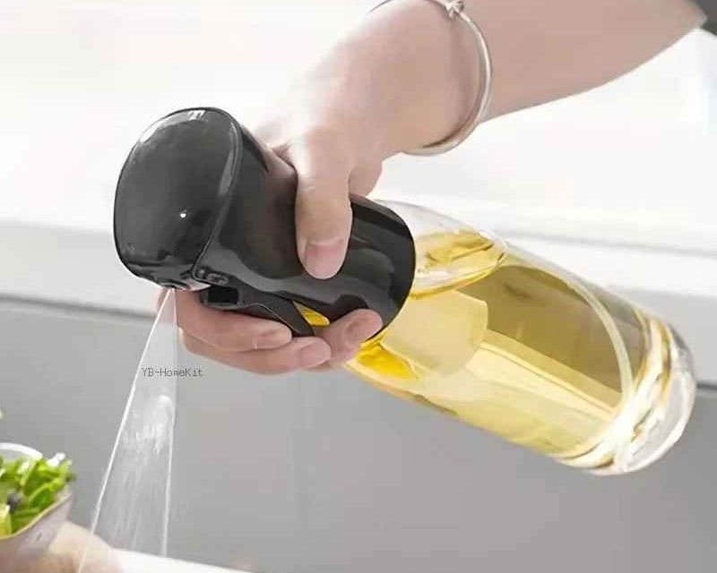 Person using a handheld sprayer to mist a bottle of olive oil over food on a kitchen counter.