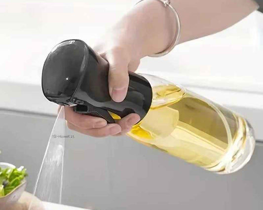 Person using a handheld sprayer to mist a bottle of olive oil over food on a kitchen counter.